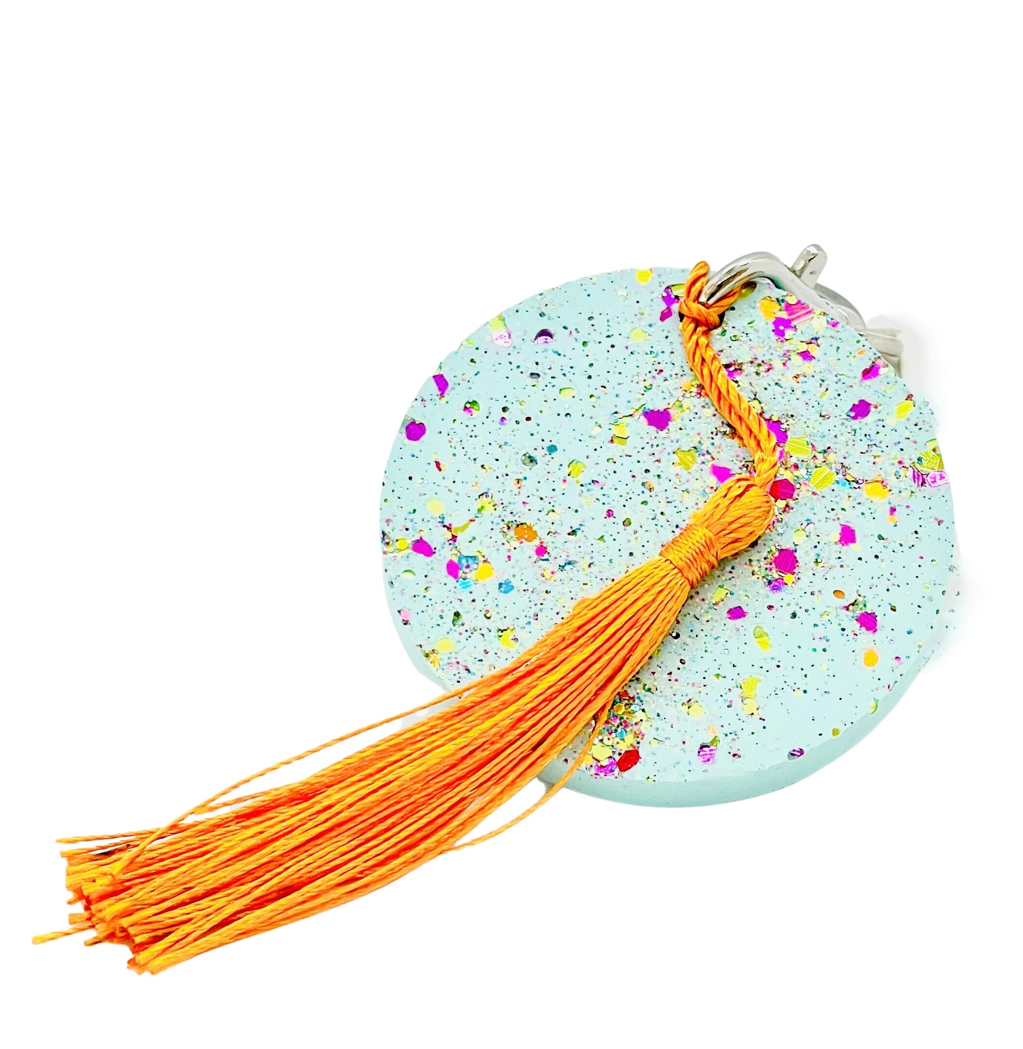 A round Jesmonite disc keyring measuring 6cm in diameter coloured with turquoise pigment and sprinkled with rainbow glitter.