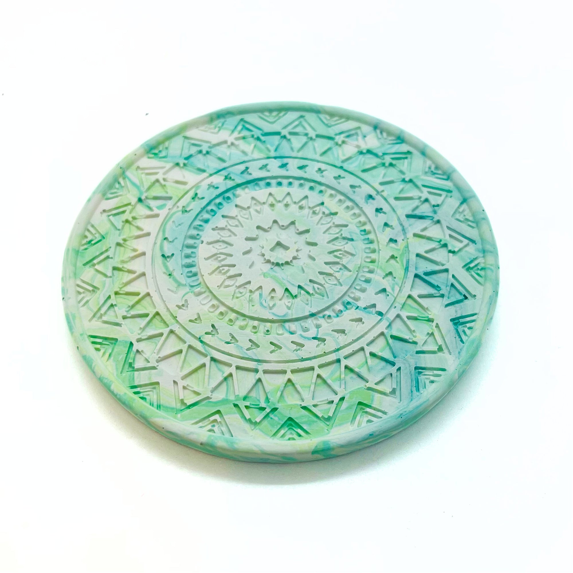 A circular mandela Jesmonite coaster measuring 9.3cm in diameter and 0.8 cm in height marbled with turquoise and lime pigment.