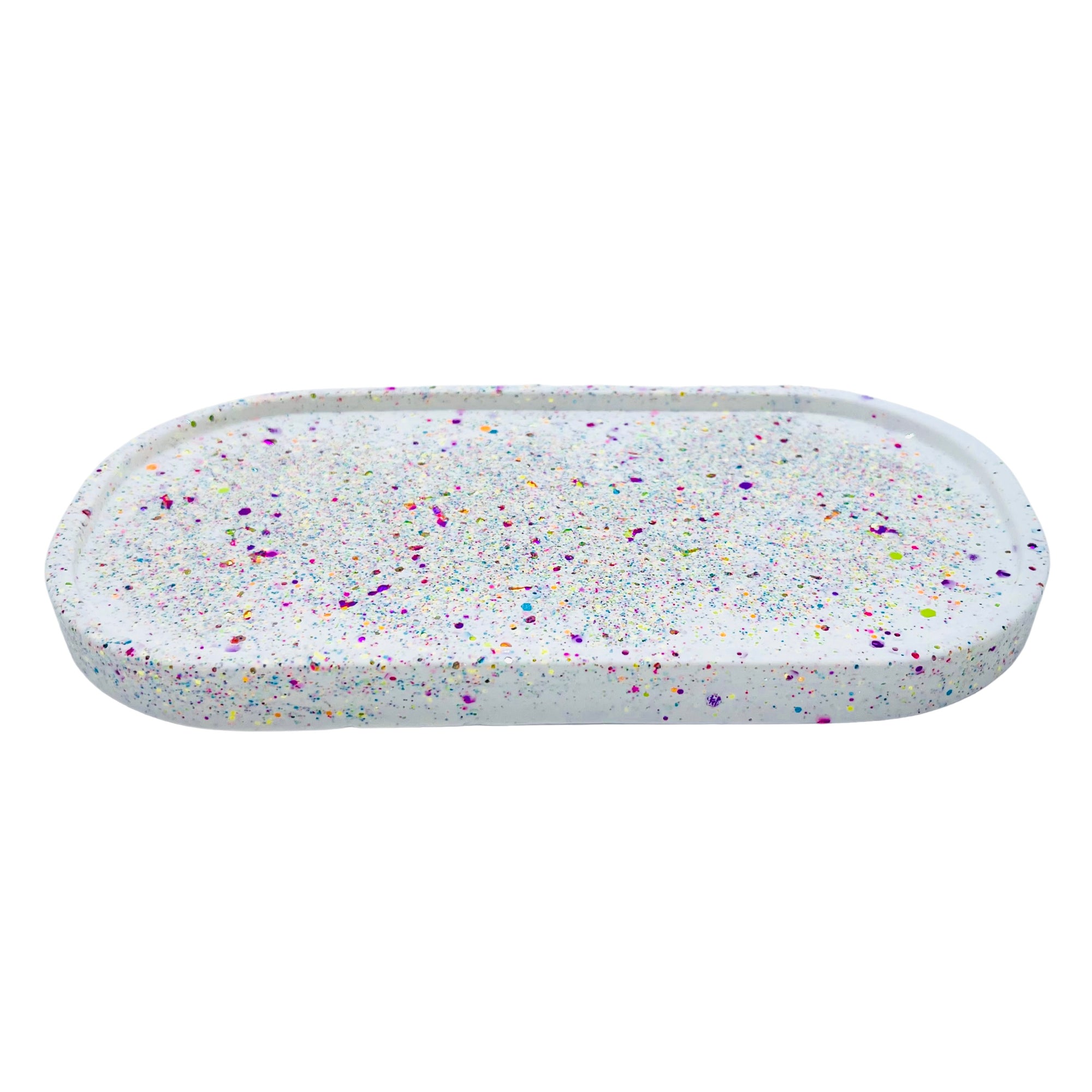 A white oval Jesmonite trinket tray sprinkled with rainbow glitter.
