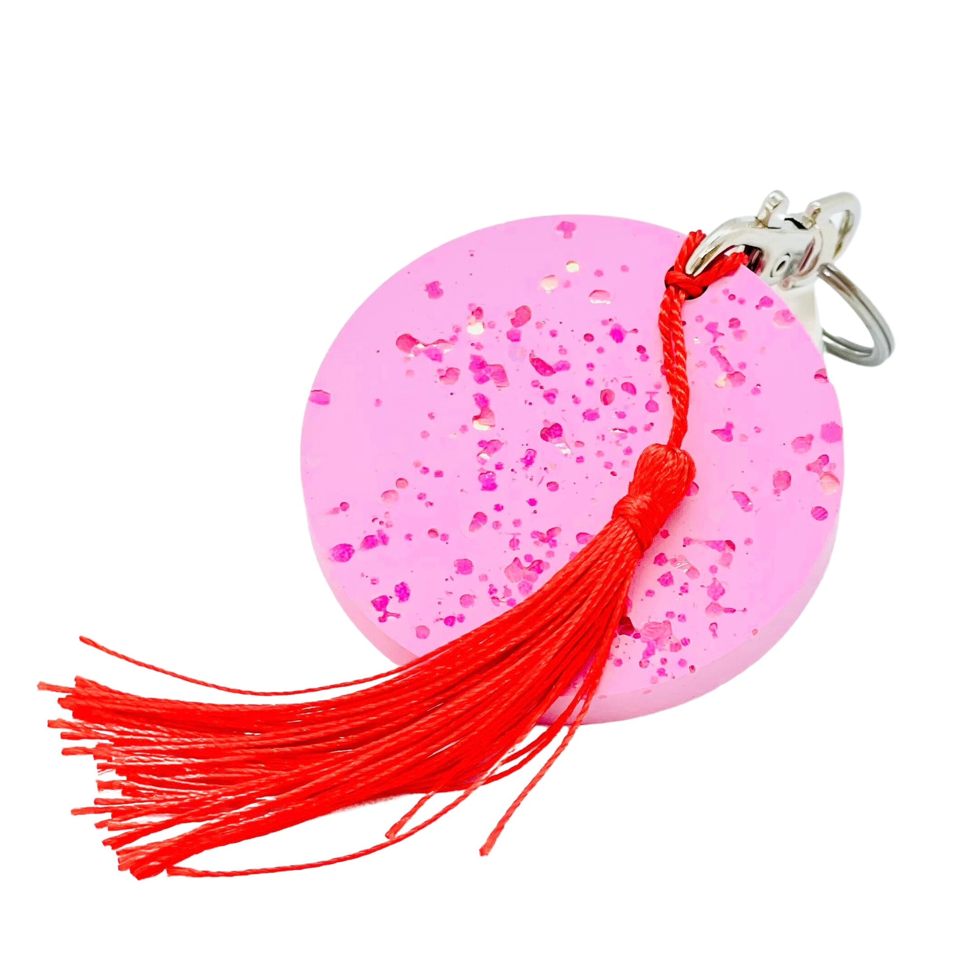 A round Jesmonite disc keyring measuring 6cm in diameter coloured with magenta pigment and sprinkled with pink glitter.