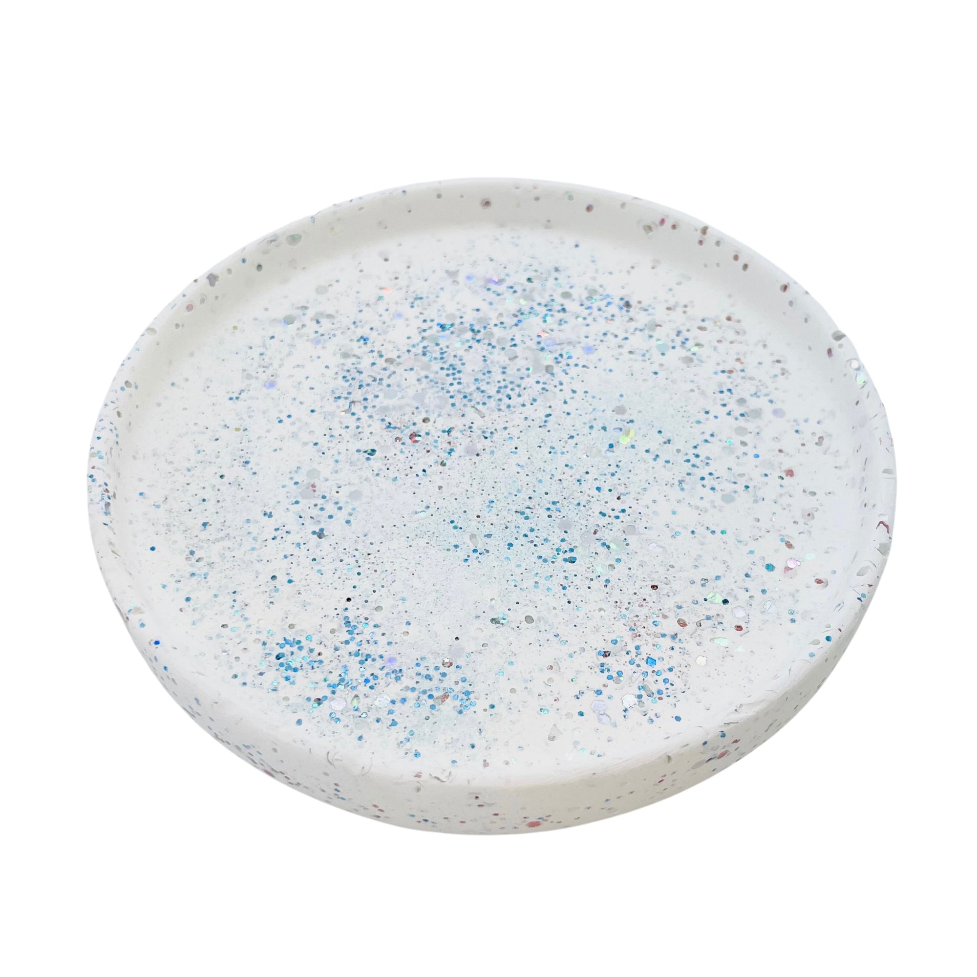 A  circular white Jesmonite trinket tray measuring 15.4cm in diameter sprinkled with blue glitter.